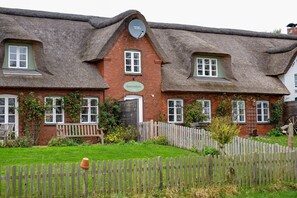 A traditional brick house with a thatched roof, a wooden fence, and a bench.