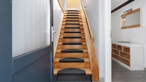 A wooden staircase with black steps and a carpeted landing, leading to a room with a white cabinet and a mirror.