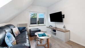 A modern living room with a black leather sofa, a small round table, a white cabinet, and a TV mounted on the wall.