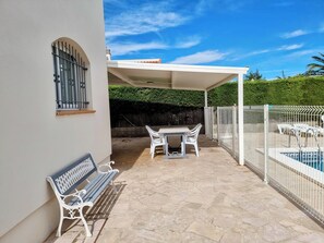 Ein überdachter Patio-Bereich mit Pool, Tisch und Stühlen sowie einer Bank.