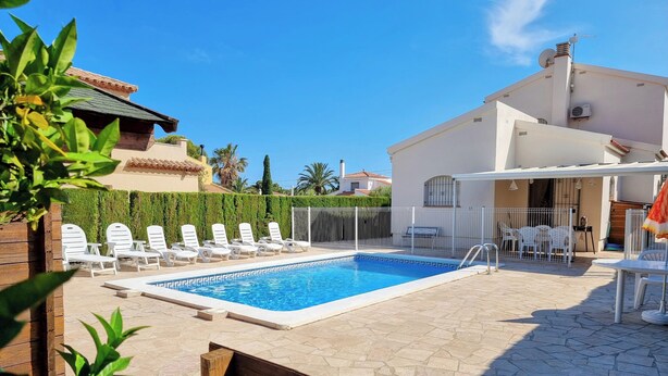 A swimming pool with lounge chairs, a wooden bench, and a white building with a covered patio area.