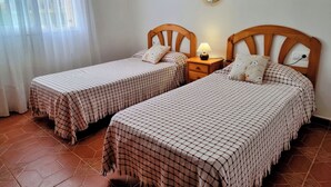 A bedroom with two beds, a nightstand, a mirror, and a window with sheer curtains.