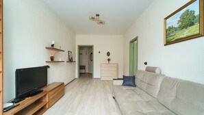 Ett vardagsrum med en platt-TV på ett träställ, en beige soffa och en tavla på väggen.
