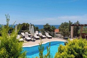 Un espace aménagé au bord de la piscine, avec des chaises longues et des parasols, donnant sur une étendue d’eau.