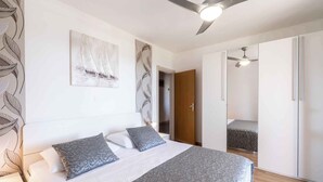 Une chambre à coucher avec un lit, un ventilateur de plafond, une porte donnant sur une autre pièce et un mur orné d’un motif de feuilles.