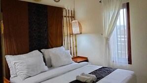 Una cama bien tendida con ropa blanca, un panel decorativo en la pared, una lámpara colgante y una ventana con cortinas.