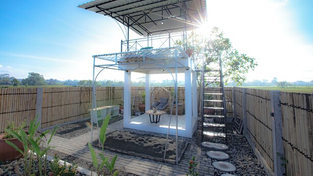 Un espacio de estar al aire libre cubierto, con una mesa y sillas, rodeado por una valla de madera y un jardín.