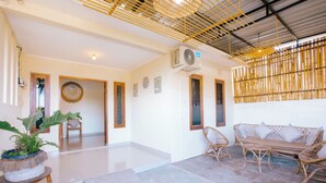 Una habitación amplia con techo alto, un equipo de aire acondicionado grande, una pantalla de bambú, un conjunto de sofás y una planta en maceta.