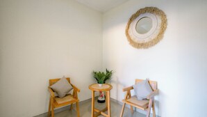 Habitación de esquina con dos sillas de madera, una pequeña mesa redonda con una planta en maceta y un espejo montado en la pared.
