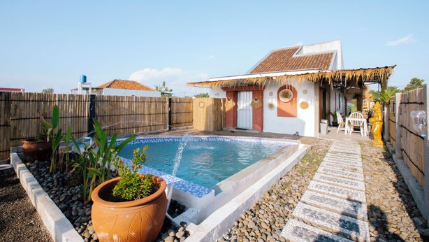 A backyard with a swimming pool, a house with a thatched roof, and a small patio area. -  Villa New D'Bamboo by Plesirhatiyogja (Sewon)