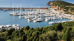 Un puerto deportivo con numerosas embarcaciones amarradas, un pequeño edificio y terreno rocoso al fondo.