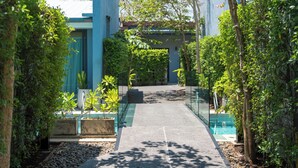 A pathway leading to a building with a blue exterior, surrounded by greenery and a pool area. - Xen Pool Access (Rawai)