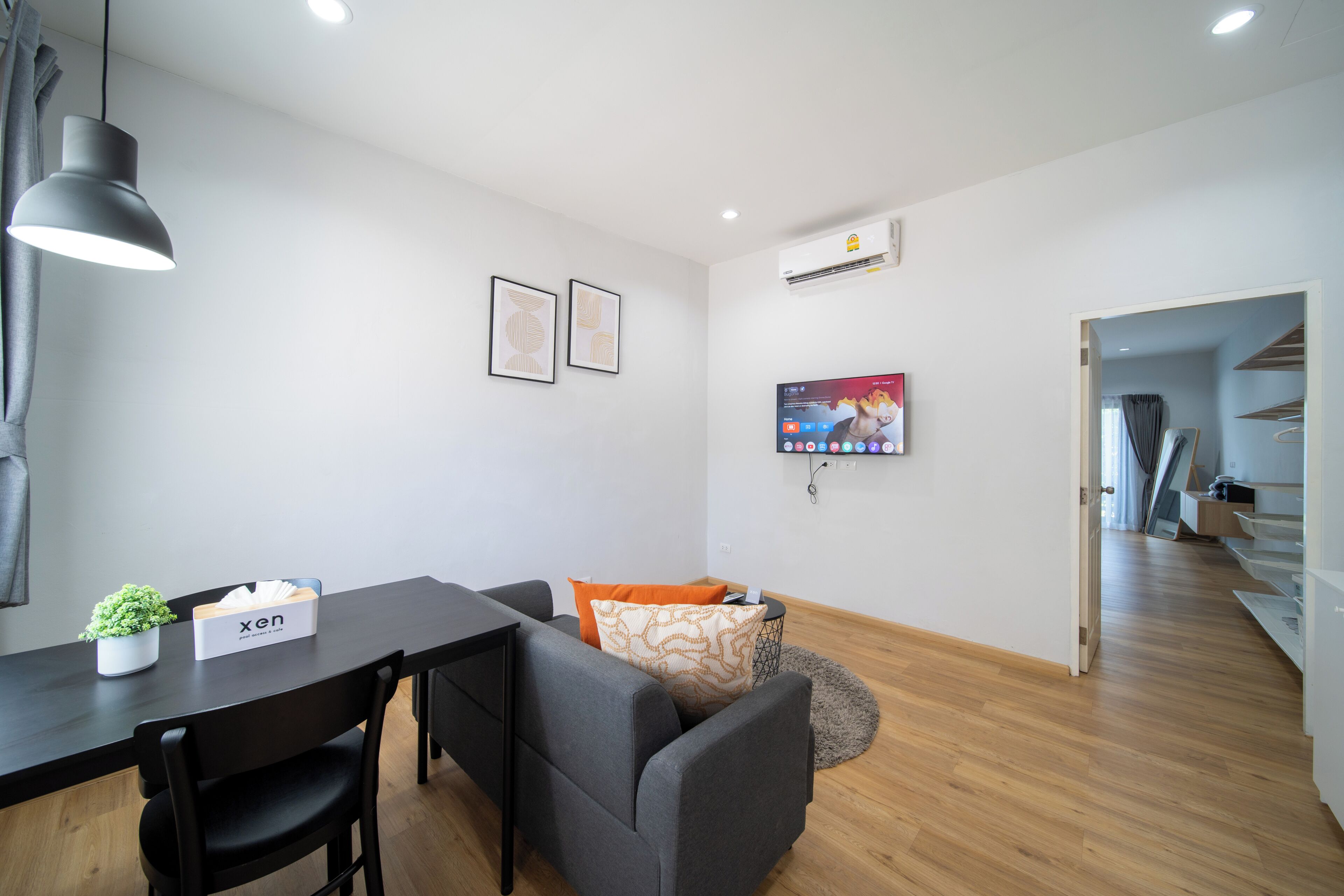 A modern living room with a dining table, grey sofa, and a TV mounted on the wall.