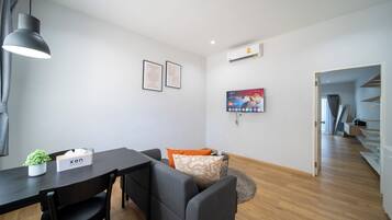 A modern living room with a dining table, grey sofa, and a TV mounted on the wall.