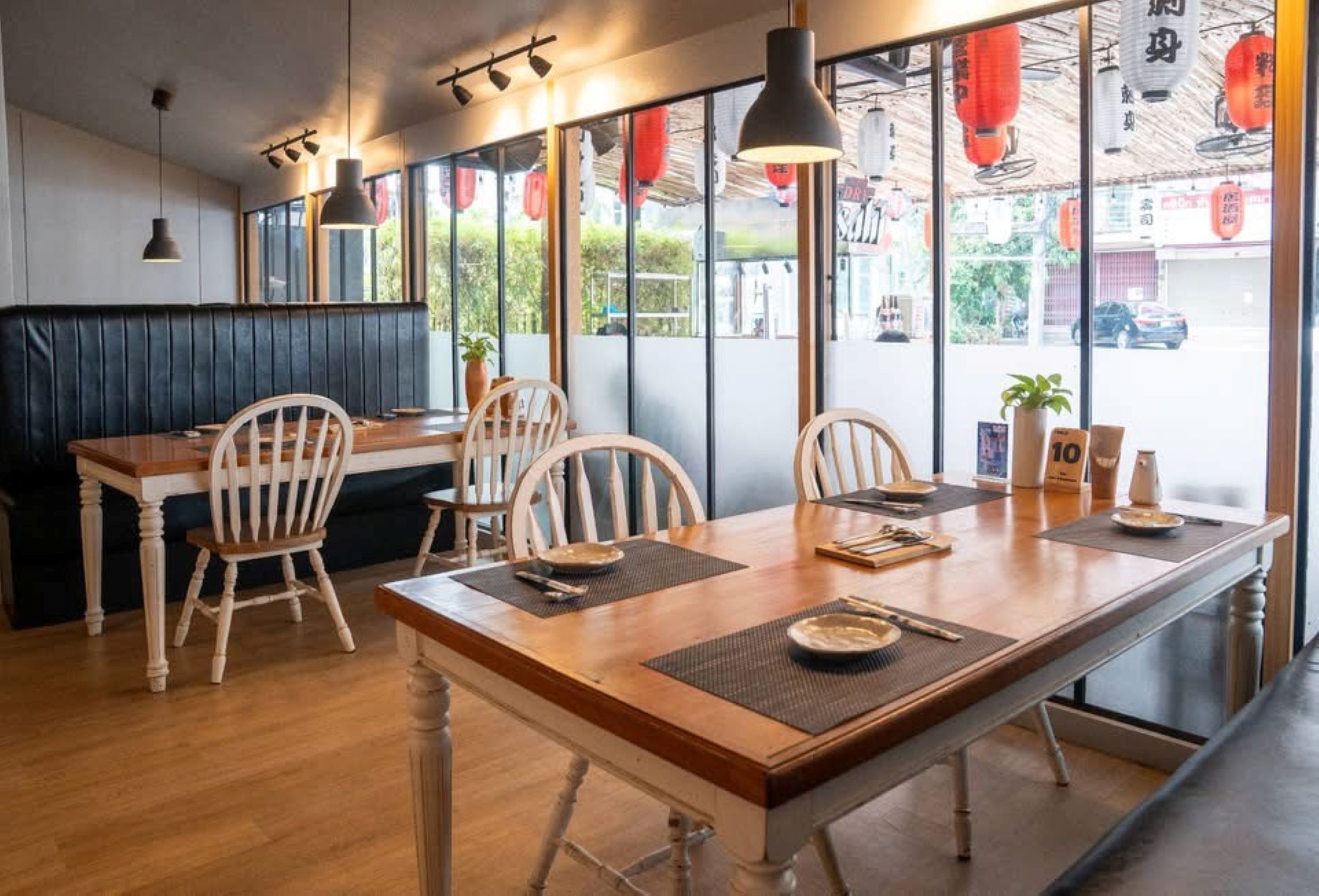A restaurant interior with a wooden dining table, chairs, and a booth seating area.