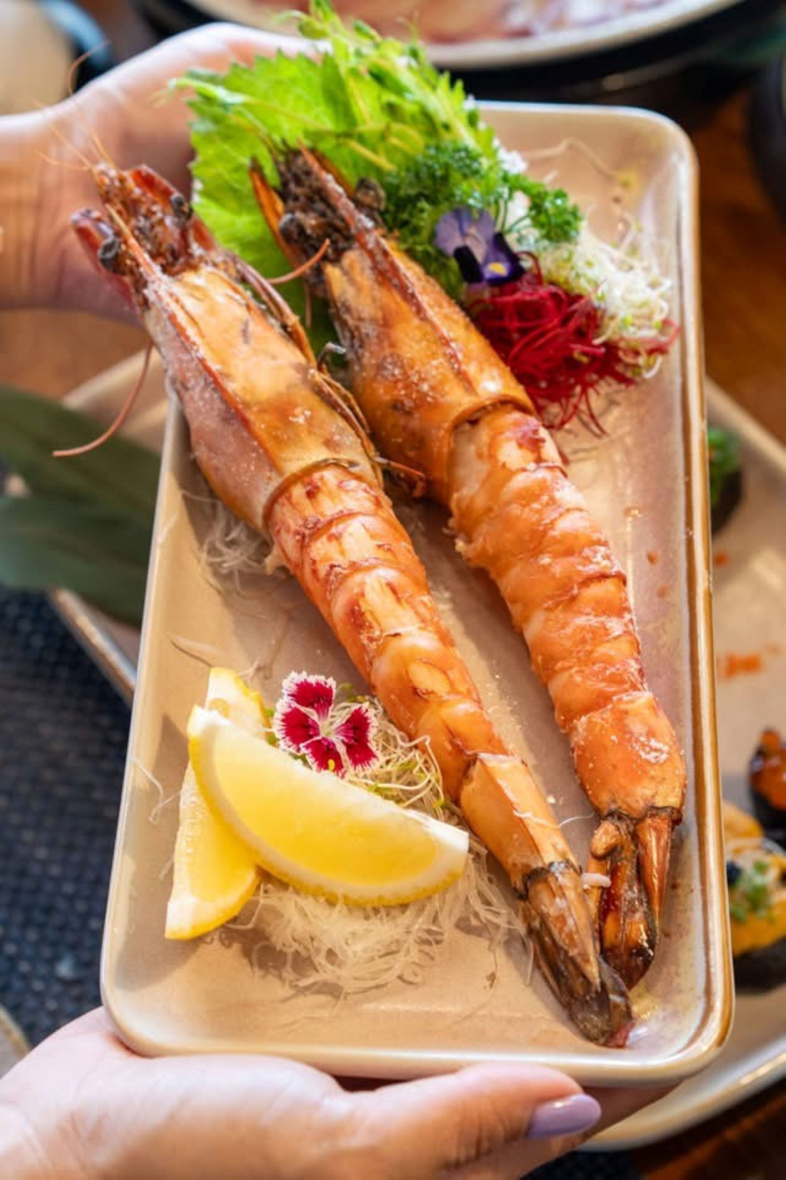 A tray with two cooked shrimp, lemon wedges, and some greens.