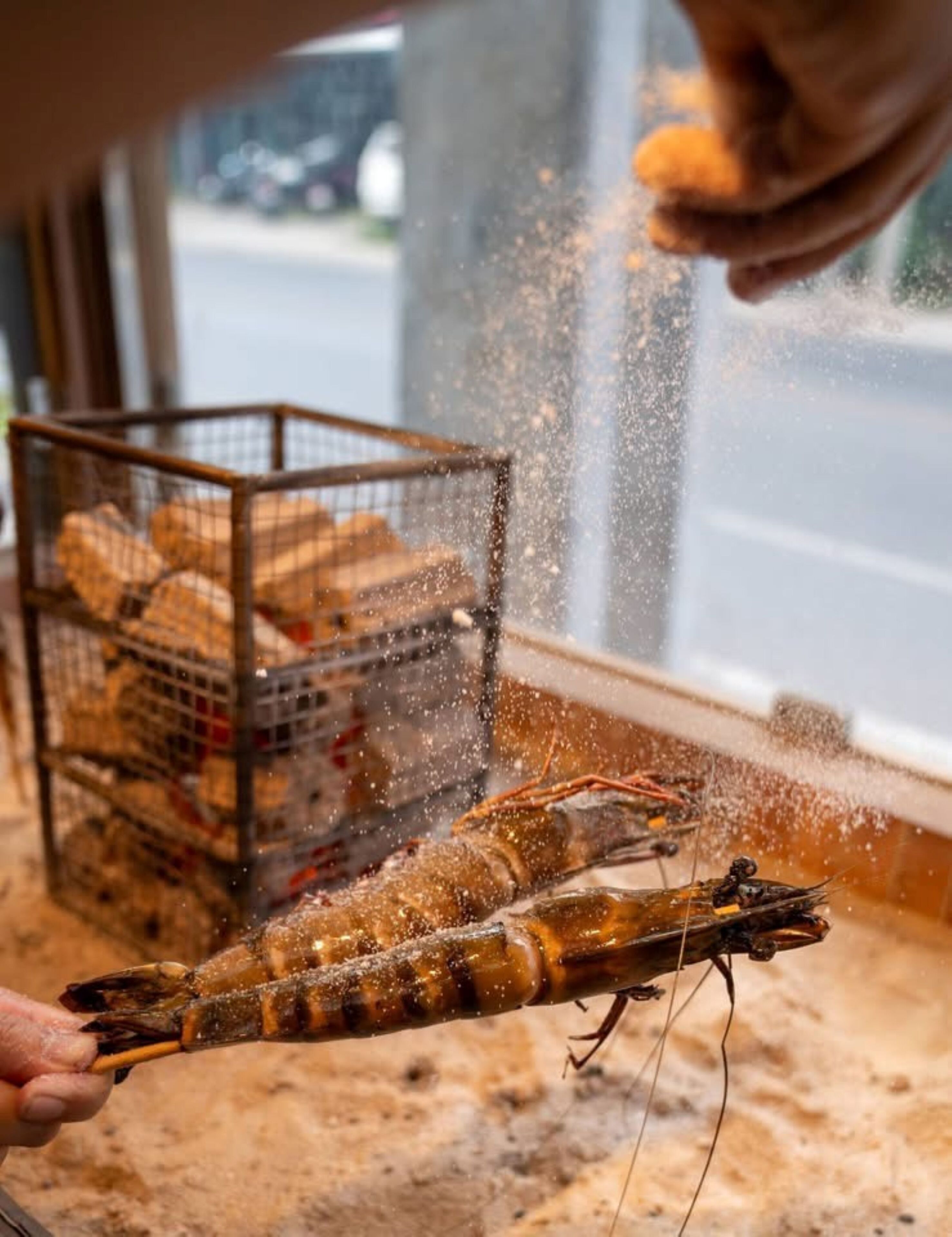 A person holding a shrimp with a salt shaker nearby.