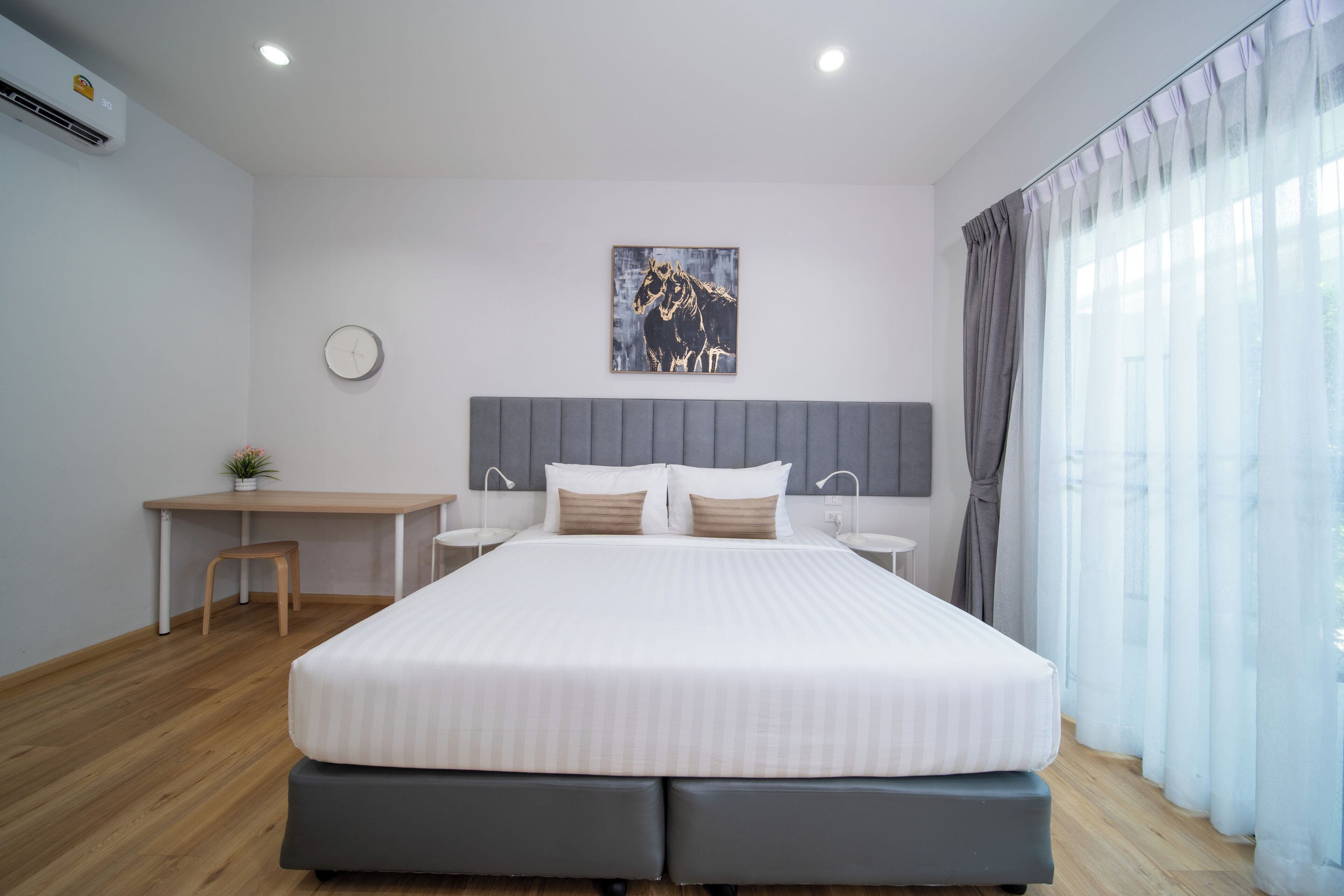 Une chambre moderne avec un grand lit, un bureau et une chaise, une horloge au mur et une fenêtre avec des rideaux.