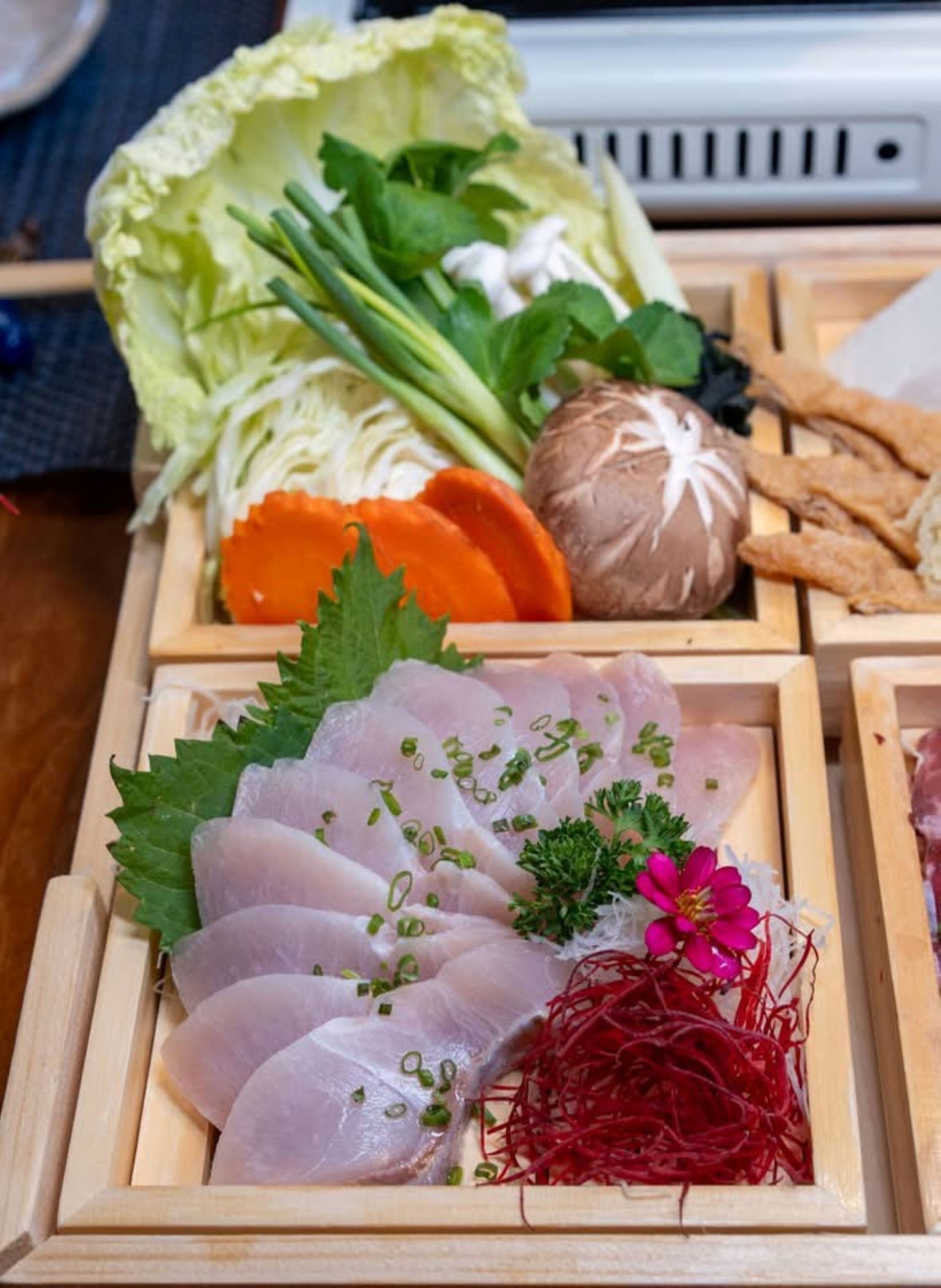 A wooden tray with various food items including sashimi, vegetables, and a decorative flower.