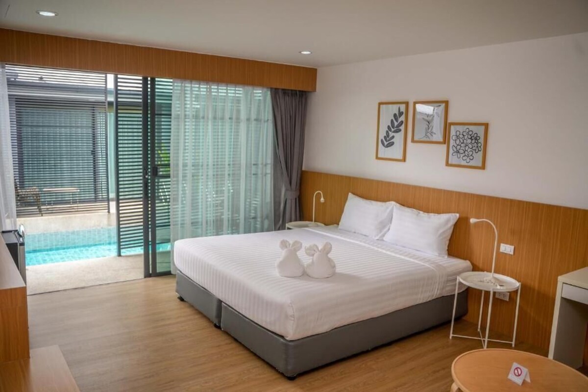 A hotel room with a bed, a small table, a chair, a window with blinds, and a view of a pool.