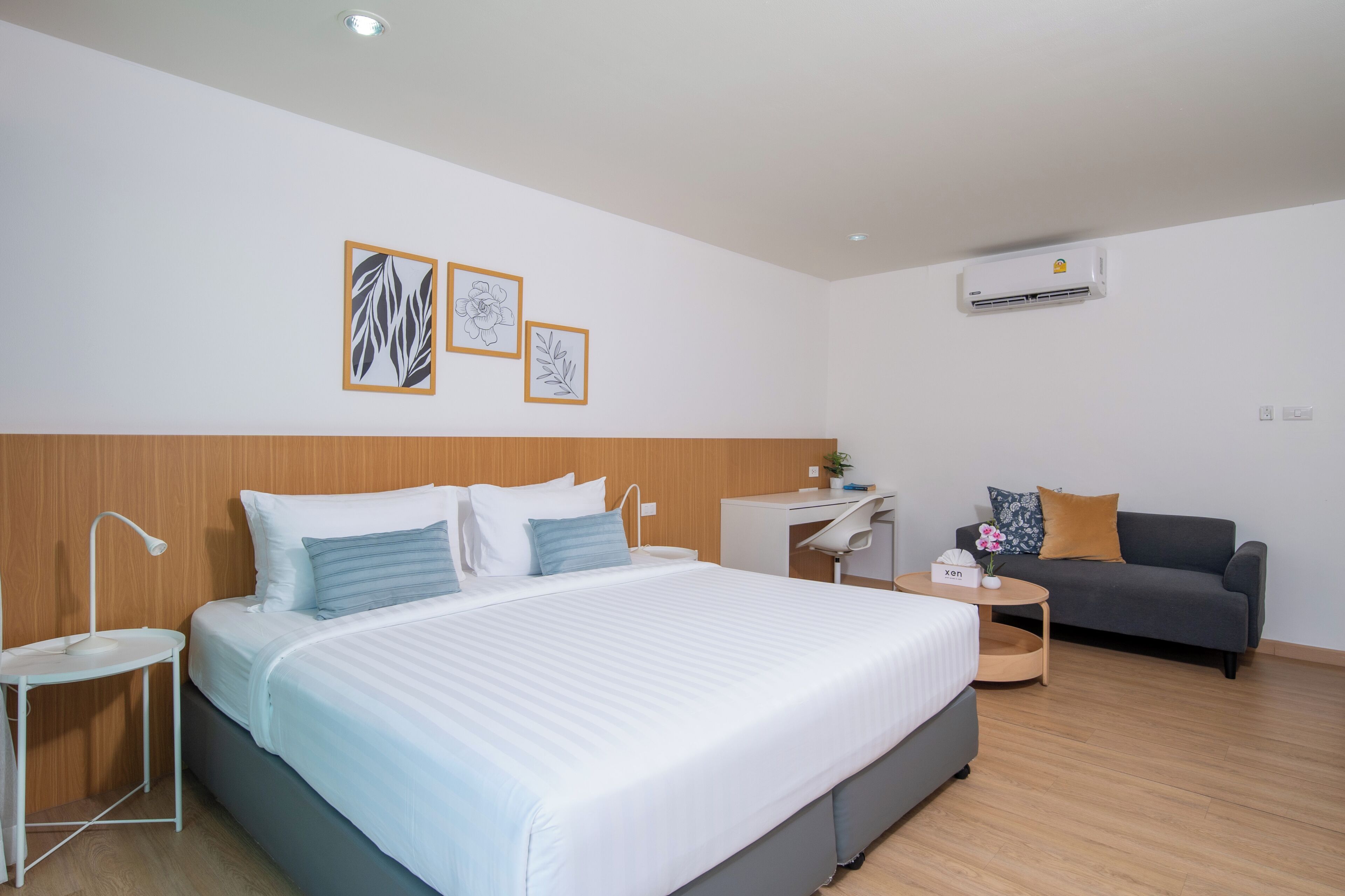 A modern hotel room with a large bed, a desk, a sofa, and an air conditioning unit.
