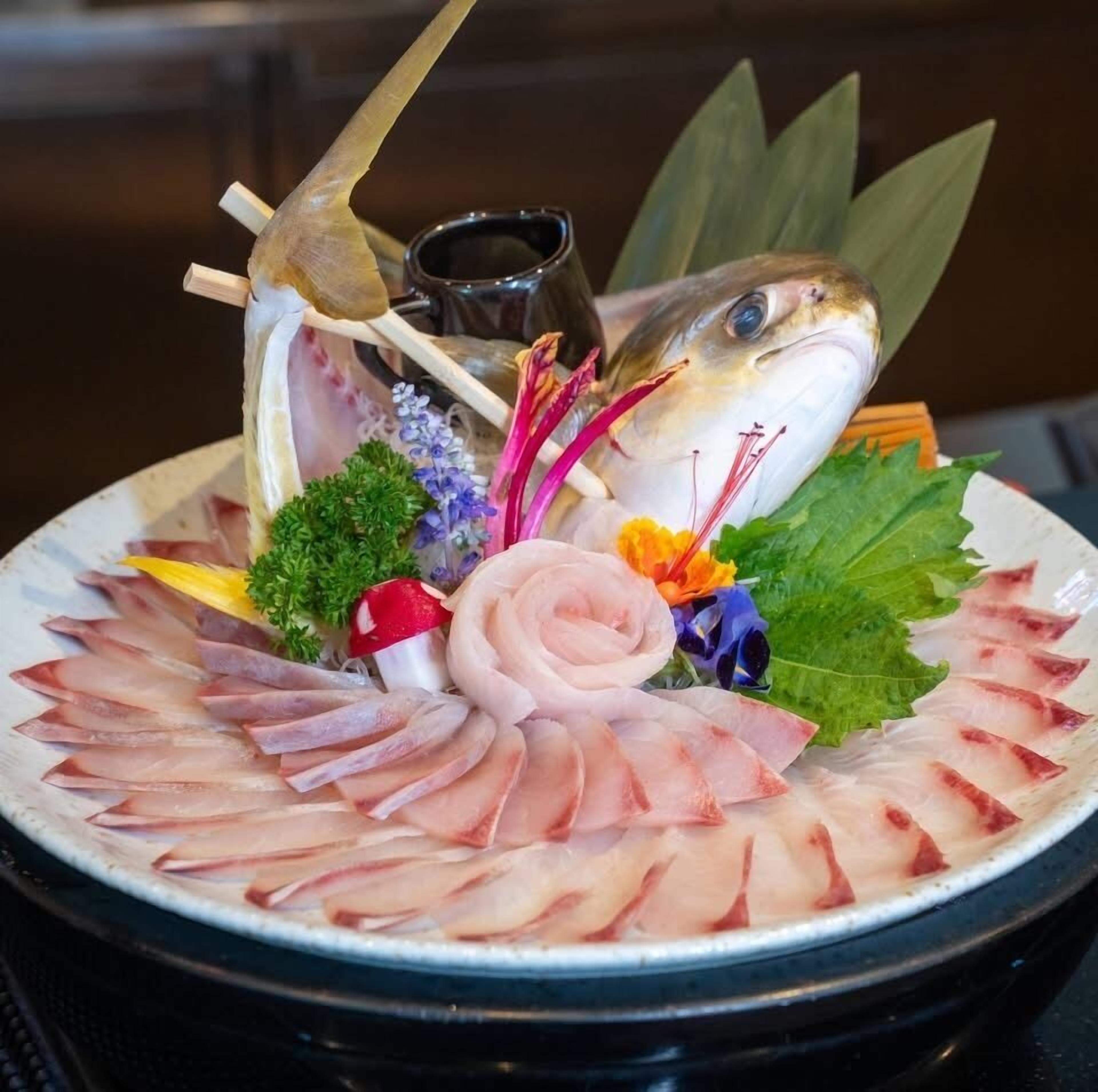 A plate of sashimi with a decorative arrangement including flowers and a wooden chopstick.