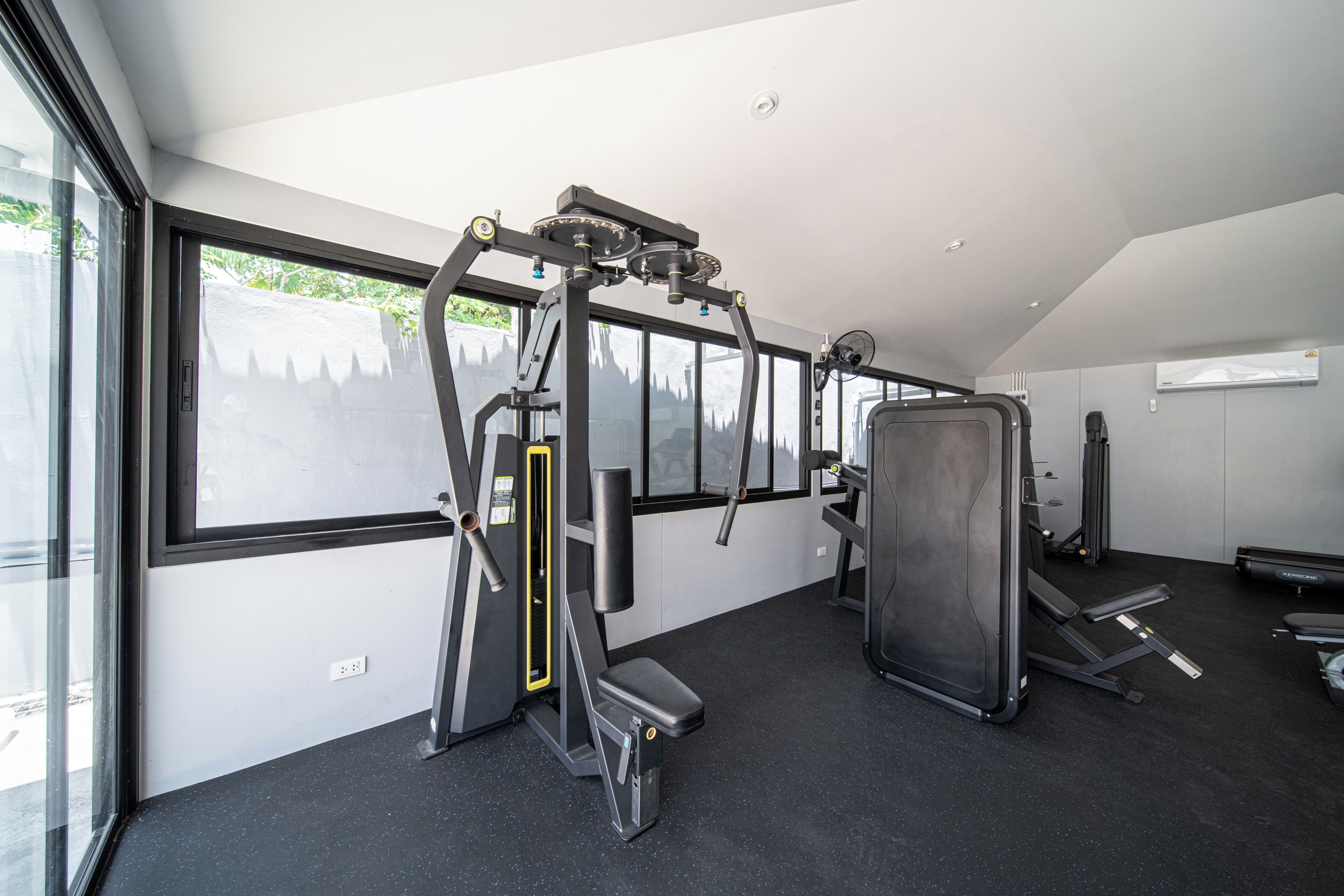 Un gimnasio con equipo de ejercicio, ventanas amplias y suelo negro.