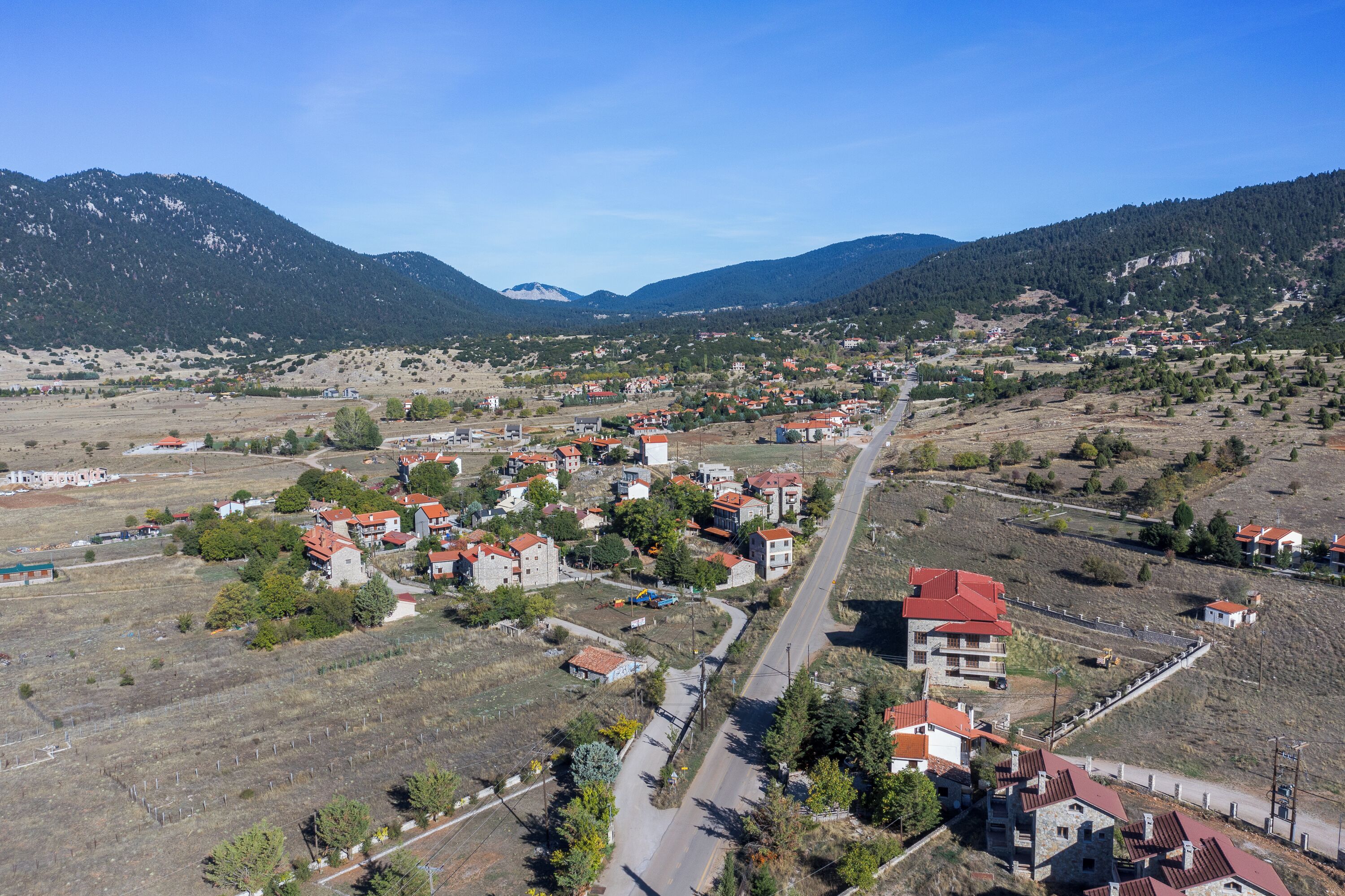 A town with a main road, buildings with red roofs, and mountains in the background.