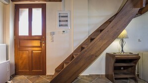 Un escalier en bois mène à une porte dotée d’un panneau en verre dépoli. On peut voir une boîte électrique fixée au mur et une petite étagère sur laquelle se trouve une lampe.