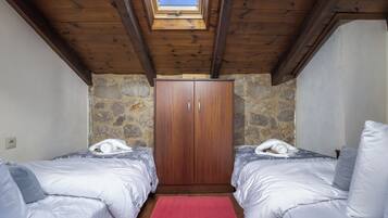 A small, cozy bedroom with two beds, a wooden wardrobe, and a skylight.