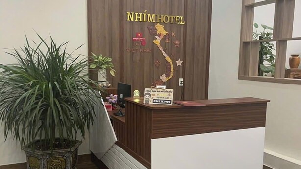 Un mostrador de recepción con diseño de panel de madera, una planta en maceta y un mapa de Vietnam colgado en la pared.