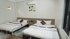 Habitación de hotel con dos camas, una alfombra gris y mullida, suelo de madera, aire acondicionado montado en la pared y un ventanal.