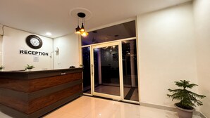 A reception area with a wooden reception desk, a wall clock, and a large sliding glass door leading to a balcony. - The Kiaan Corbett Resort (Ramnagar)