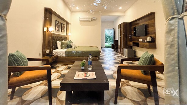 A hotel room with a bed, a TV, a small table with a bottle and a menu, and a patterned floor. - The Kiaan Corbett Resort (Ramnagar)