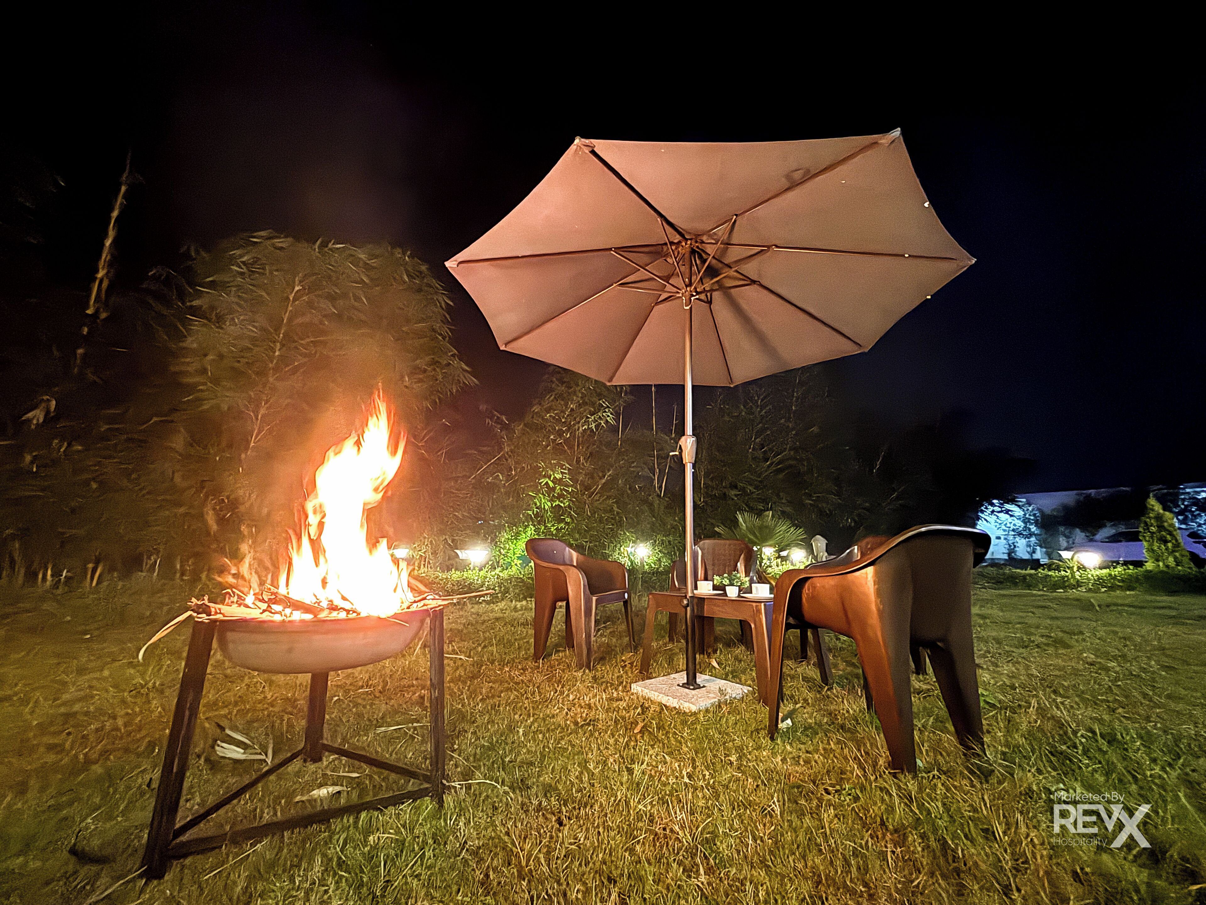 A night scene with a campfire, outdoor furniture, and an umbrella.