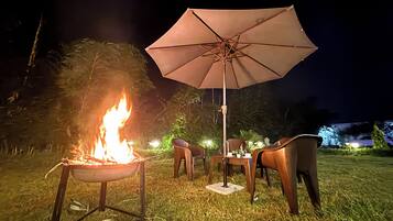 A night scene with a campfire, outdoor furniture, and an umbrella.