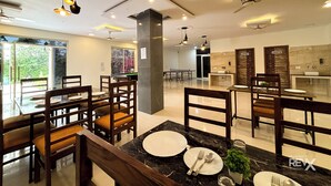 A modern dining area with wooden chairs and tables, a ping pong table, and a view of greenery outside. - The Kiaan Corbett Resort (Ramnagar)