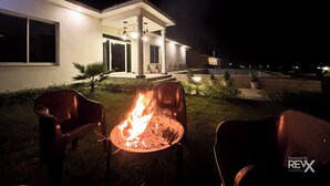 A modern house with a fire pit in the yard, two chairs, and a well-lit entrance. - The Kiaan Corbett Resort (Ramnagar)
