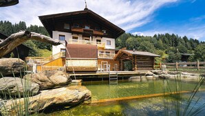 Ein traditionelles Holzchalet mit Balkon, Teich und bewaldeter Kulisse.