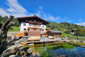 A chalet-style building with a wooden deck and a small pond.
