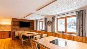 Ein Holzinterieur mit Essbereich, einem an der Wand montierten Fernseher und großen Fenstern mit Vorhängen.