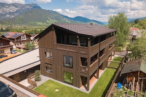 A modern multi-story building with balconies, a flat roof, and a view of mountains.