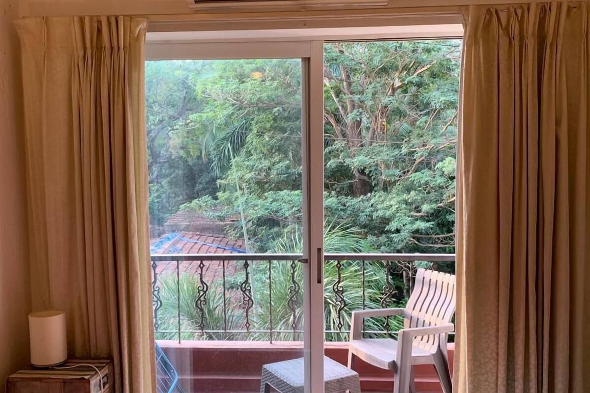 Quarto com cama, mesa de cabeceira, abajur e vista para uma varanda com uma cadeira.