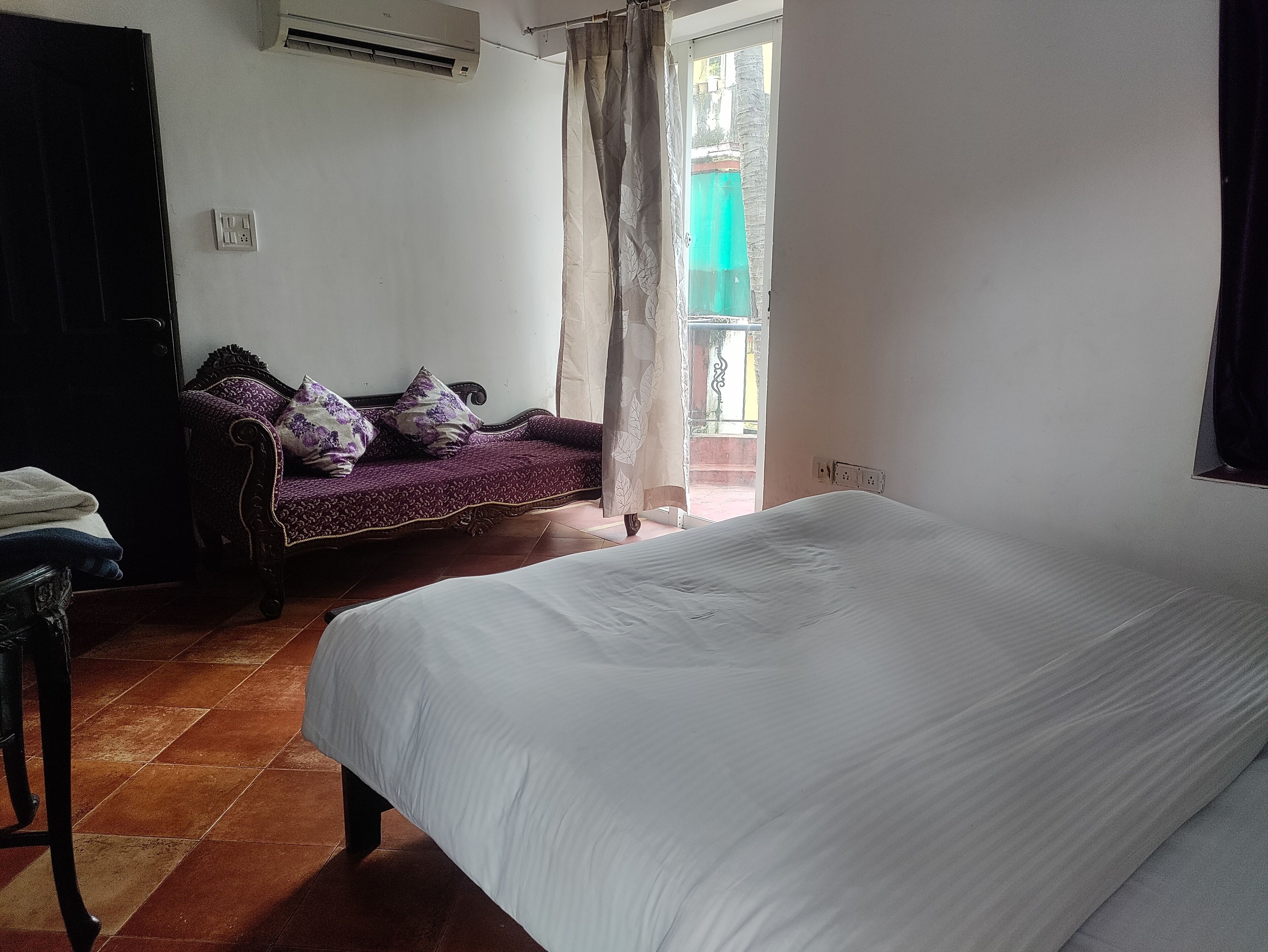 A bedroom with a bed, a sofa, a chair, and a window with curtains.