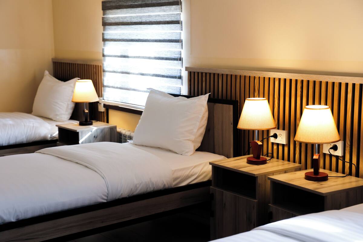 A hotel room with two beds, each with white bedding and lamps on wooden nightstands.