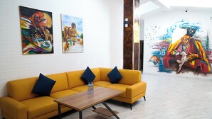 Een moderne hotel lobby met een gele bank, een houten salontafel en twee schilderijen aan de muur.