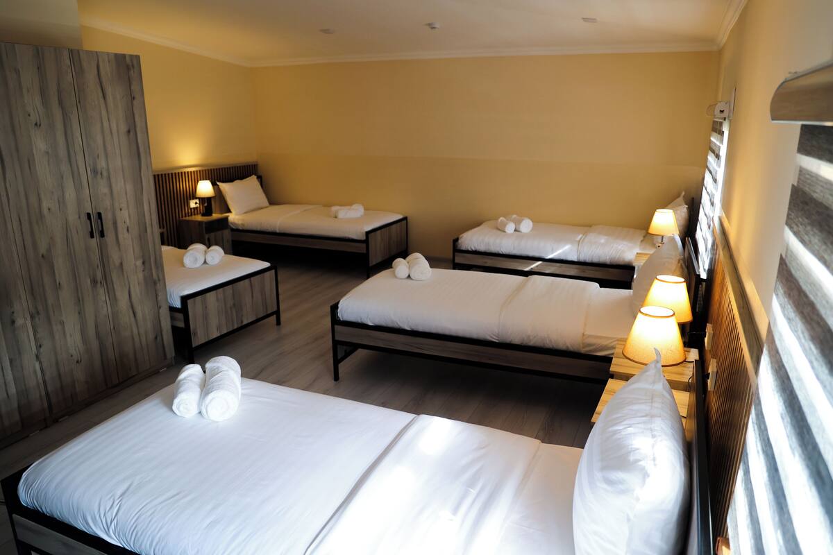 A hotel room with three single beds, each with white linens and towels, wooden headboards, and bedside lamps.