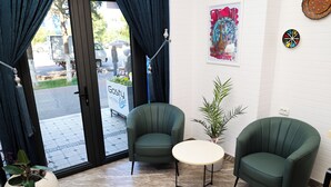 Een kamer met twee groene fauteuils, een kleine ronde tafel, een potplant en een bord met Hotel Gossty erop.