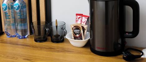 A kitchen counter with a coffee maker, two water bottles, a glass mug, and coffee pods.