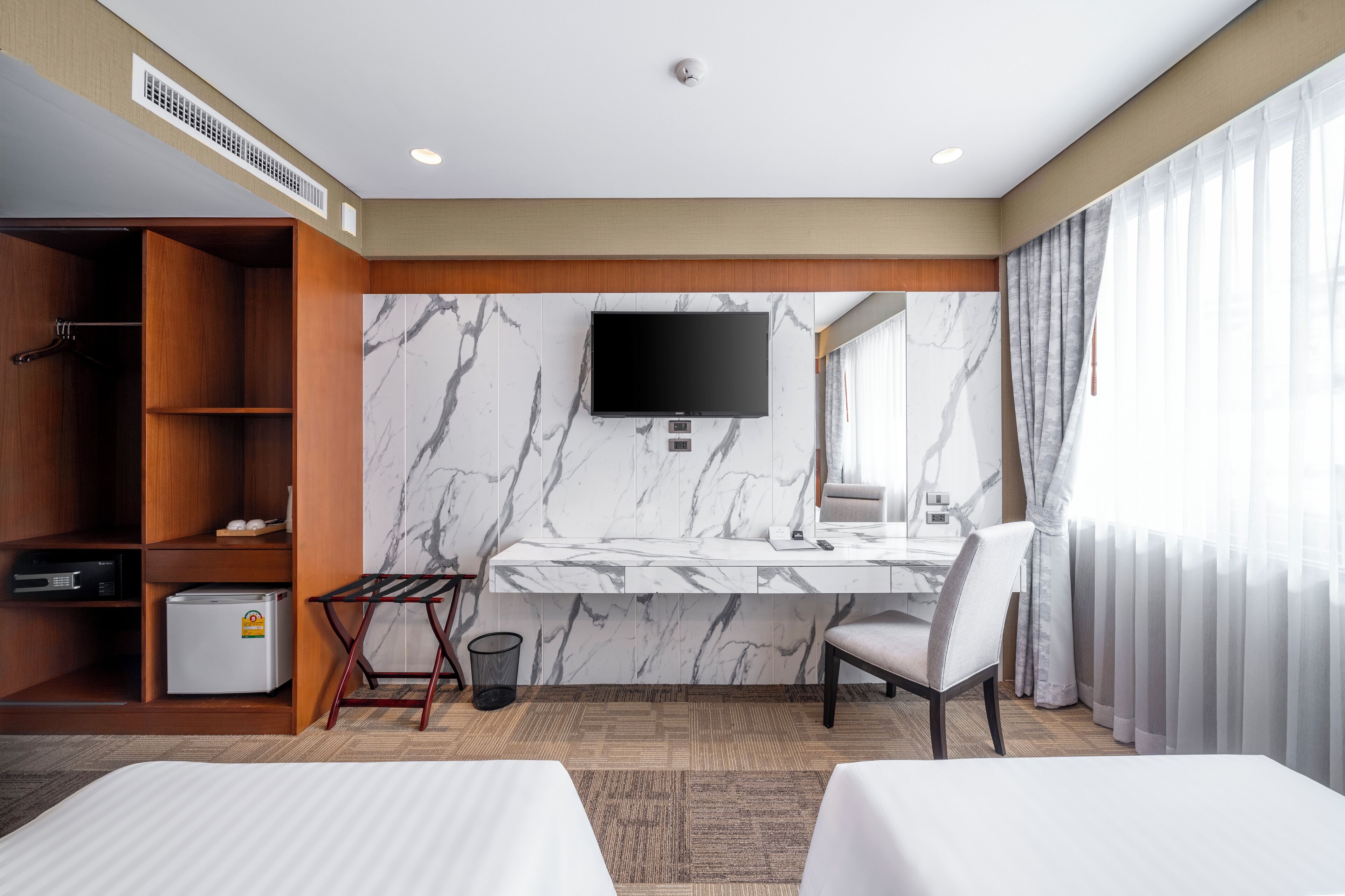 Habitación de hotel con cama, escritorio con televisor, armario, refrigerador pequeño y baño con espejo y cortinas.